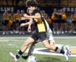 High school soccer players compete for the ball under stadium lights, showcasing athleticism and teamwork during the game.