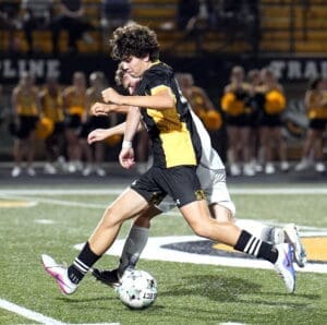 High school soccer players compete for the ball under stadium lights, showcasing athleticism and teamwork during the game.