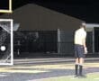 A soccer goalie dives to stop a penalty kick during a night match, with players and referees in the background.