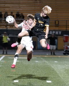 Two soccer players compete for the ball during a nighttime match, showcasing intense athleticism and teamwork.