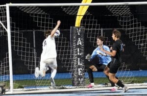 A soccer player leaps to score as the goalie prepares to block the shot, capturing the game's intense moment.