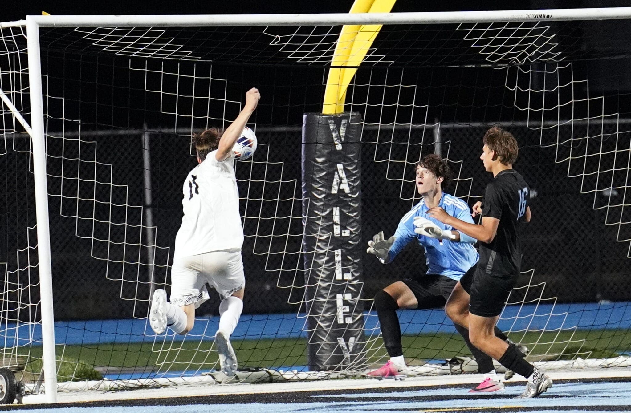 A soccer player leaps to score as the goalie prepares to block the shot, capturing the game's intense moment.
