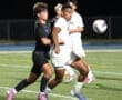 Two young soccer players compete for the ball on a field during a nighttime game. Intense action captured in motion.