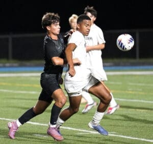 Two young soccer players compete for the ball on a field during a nighttime game. Intense action captured in motion.