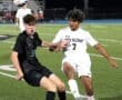 High school soccer players competing for the ball on a field under stadium lights at night.