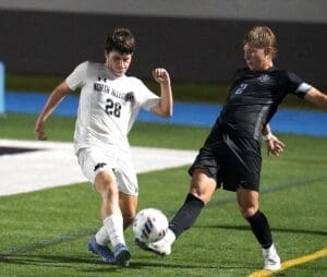 Two soccer players contest the ball during a night game, showcasing athleticism and competition on the field.