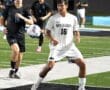 Two high school soccer players compete on the field, with one in white and the other in black, focused on the ball.