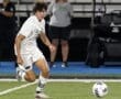 Young male soccer player in a white uniform sprinting towards the ball on a field during a match.