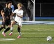Two high school soccer players compete for the ball on a well-lit field during a night game, showcasing athleticism and teamwork.