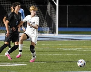 Two high school soccer players compete for the ball on a well-lit field during a night game, showcasing athleticism and teamwork.