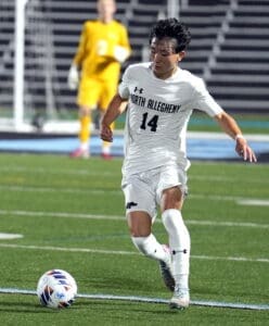 North Allegheny soccer player #14 dribbles the ball during a night game on a well-lit field.