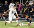 High school soccer players compete for the ball on a field during a night game, showcasing athleticism and teamwork.