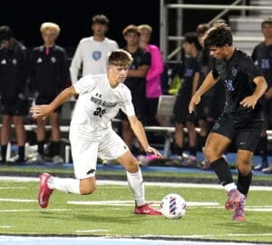 High school soccer players compete for the ball on a field during a night game, showcasing athleticism and teamwork.