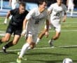High school soccer players sprinting for the ball during a night game on a well-lit field.