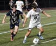 High school soccer match: North Allegheny player competes for the ball against a Butler opponent on the field.