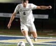 North Allegheny soccer player in white jersey dribbling a ball on the field during a night match.