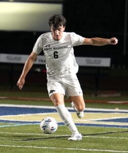 North Allegheny soccer player in white jersey dribbling a ball on the field during a night match.