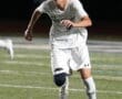 Young soccer player sprinting on the field, focused on the ball during an evening match.