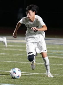 Young soccer player sprinting on the field, focused on the ball during an evening match.