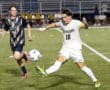 North Allegheny soccer player in white kicks the ball, while a Butler player in blue pursues, during a competitive match.