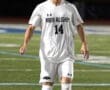 A soccer player in a white North Allegheny jersey dribbles a ball on a field at night.