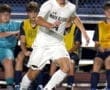 North Allegheny soccer player dribbles the ball during a night game, with teammates watching from the sidelines.