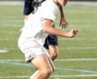 Teenage soccer players in action on the field, one dribbling a ball while another defends.