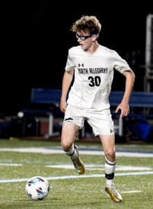 North Allegheny soccer player in action, dribbling the ball on a well-lit field during a night game.