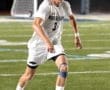 A soccer player in a white jersey dribbles a ball on a field at night, showcasing athleticism and focus.