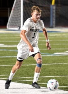 A soccer player in a white jersey dribbles a ball on a field at night, showcasing athleticism and focus.