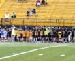 Young soccer players in colorful jerseys gather on a field, ready for practice while parents watch from the stands.