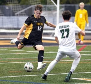 Soccer players compete fiercely on the field, with a Tiger player attempting to kick the ball past a Dragon opponent.
