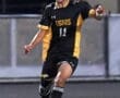 A soccer player in a black and yellow uniform, number 11, kicks a ball on a field at night.