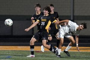 High school soccer players compete for the ball during a nighttime match, showcasing athleticism and teamwork.