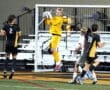High school soccer match: goalkeeper leaps to catch the ball, with players from both teams nearby on the field.