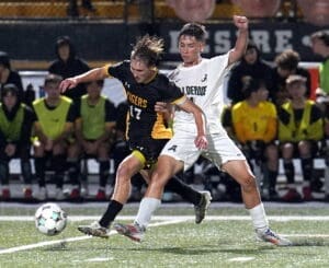 High school soccer players in action, battling for the ball under rain, showcasing athleticism and teamwork.