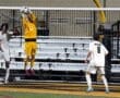 Goalkeeper in yellow leaps to catch the soccer ball during an intense game, while players in black and white watch.