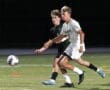 Two soccer players sprint towards the ball during a night game on a well-lit field. Action-packed sports moment.