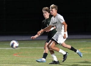 Two soccer players sprint towards the ball during a night game on a well-lit field. Action-packed sports moment.