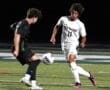 Two soccer players compete for the ball on the field during a night game, showcasing intense athleticism and teamwork.