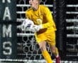 Young soccer goalkeeper in yellow uniform prepares to make a save during a night game, focused and determined.