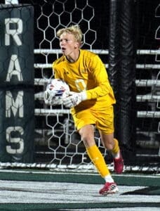 Young soccer goalkeeper in yellow uniform prepares to make a save during a night game, focused and determined.
