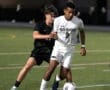 Two soccer players competing for the ball during a night game on a green field, highlighting athletic intensity.