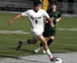 High school soccer player in action, sprinting on the field, wearing a North Allegheny uniform during a night game.