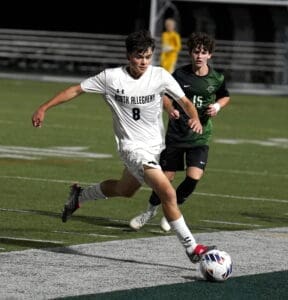 High school soccer player in action, sprinting on the field, wearing a North Allegheny uniform during a night game.