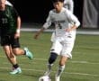 A soccer player in white, number 5, dribbles the ball on a field during a night match against an opponent.