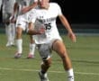 North Allegheny soccer player in action, sprinting on the field towards the ball under stadium lights.