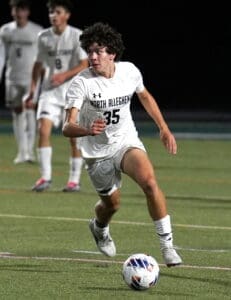 North Allegheny soccer player in action, sprinting on the field towards the ball under stadium lights.