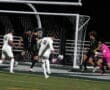 Soccer players competing for the ball near the goal during a night match on a turf field.
