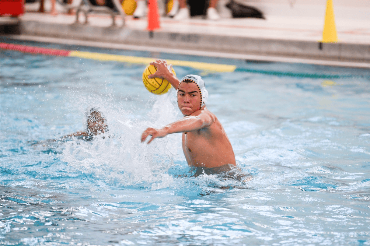 A young water polo player prepares to throw a ball in a swimming pool during a competitive game.